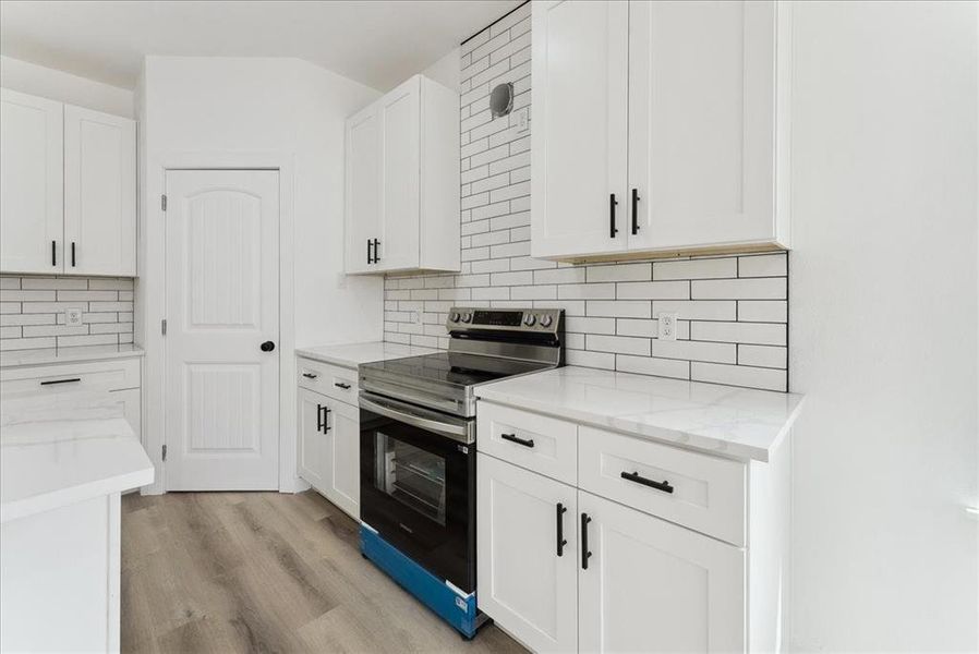 Kitchen with decorative backsplash, light stone countertops, stainless steel range with electric cooktop, light wood-type flooring, and white cabinetry