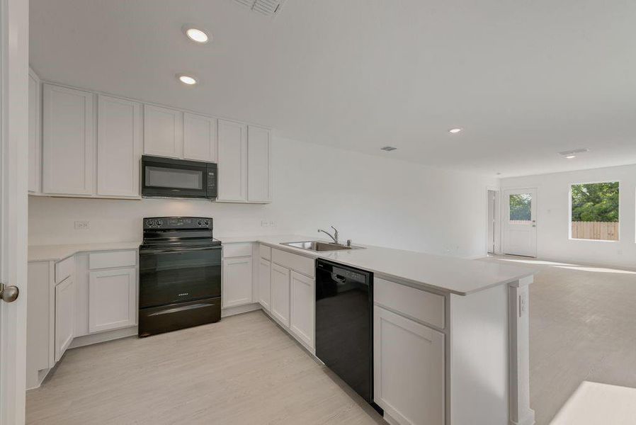 Kitchen featuring black appliances, light countertops, open floor plan, a peninsula, and white cabinetry