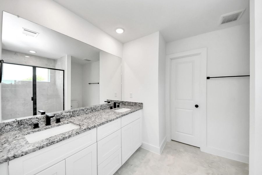 Primary Bathroom – Spacious primary bath featuring a dual-sink vanity with granite countertop, modern fixtures, large mirror, and a walk-in shower with contemporary tile surround.