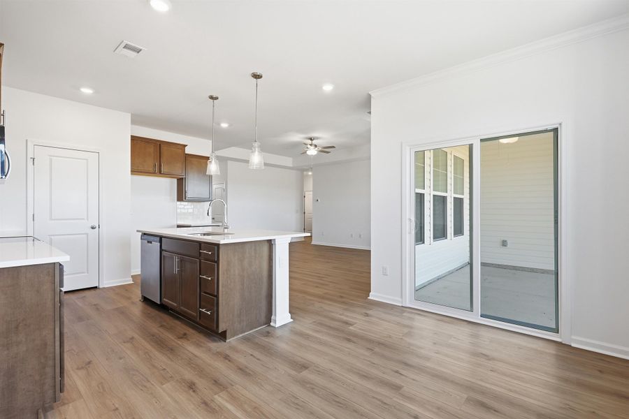 Kitchen with hanging light fixtures, a kitchen island with sink, light stone counters, open floor plan, and ceiling fan