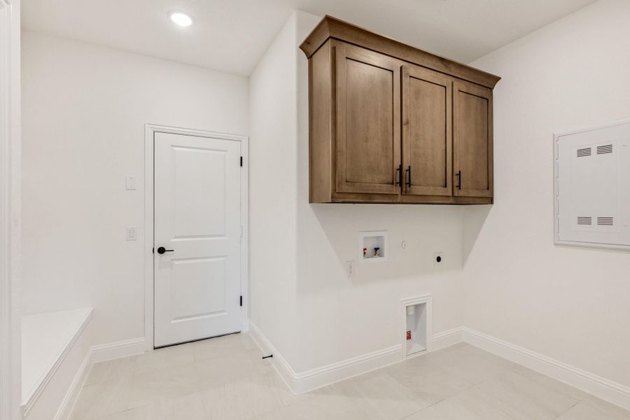 Empty laundry room with wood upper cabinets, washer and dryer hookups, and white walls