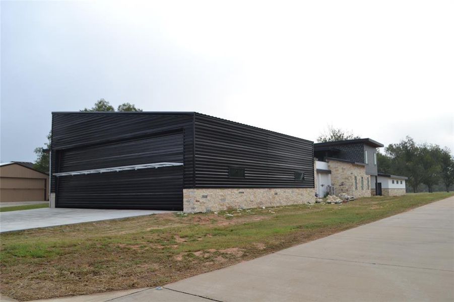View of property exterior with stone siding, a garage, and a lawn View of property exterior with stone siding, a garage, and a lawn