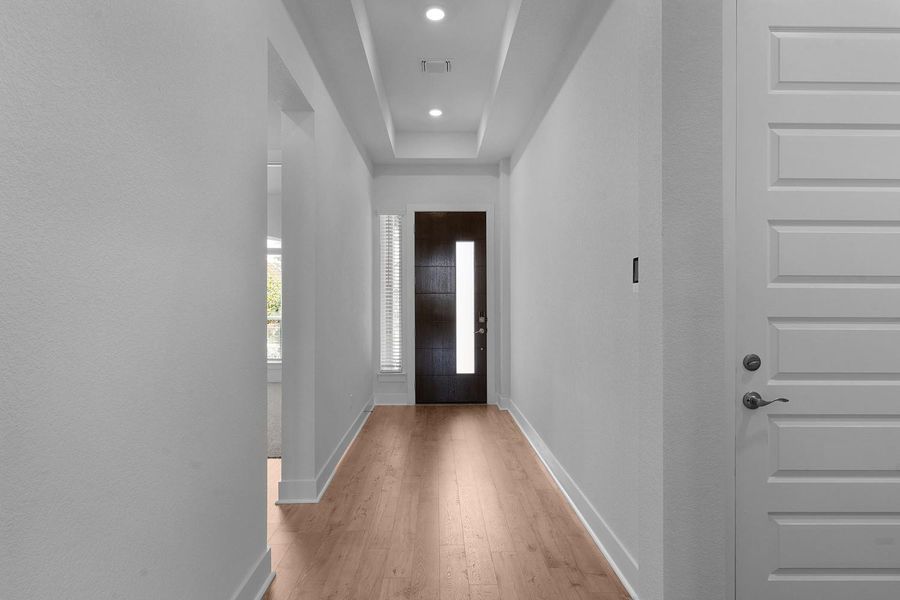 A welcoming entryway with recessed lighting and warm wood flooring extends a gracious greeting.