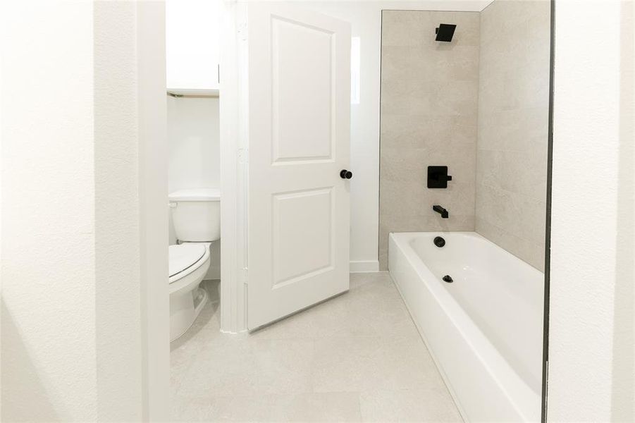 Bathroom with toilet, tile patterned floors, and tiled shower / bath