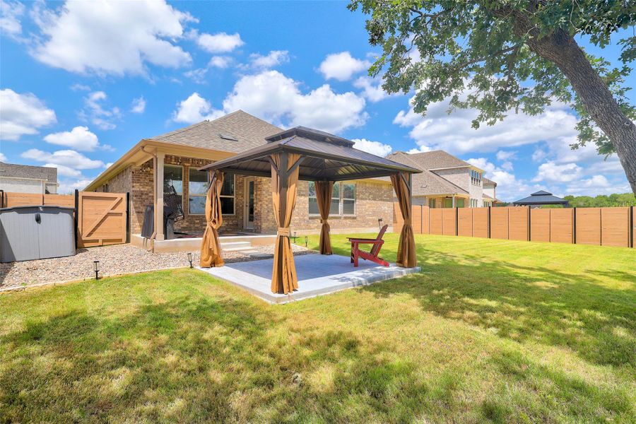 Rear view of property featuring a gazebo, brick siding, a fenced backyard, and roof with shingles