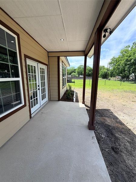 Covered concrete patio featuring brown-trimmed windows and a double French door entry