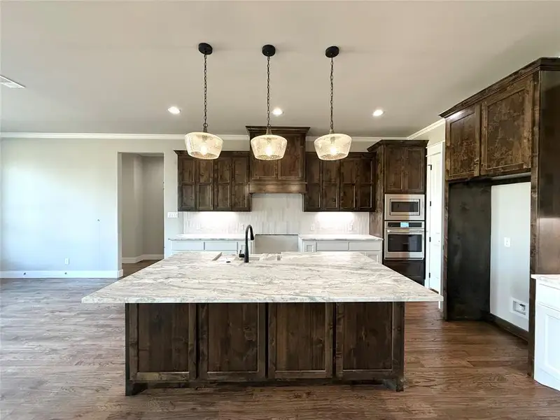 Kitchen featuring dark brown cabinetry, light stone counters, dark wood-type flooring, ornamental molding, and recessed lighting Kitchen featuring dark brown cabinetry, light stone counters, dark wood-type flooring, ornamental molding, and recessed lighting