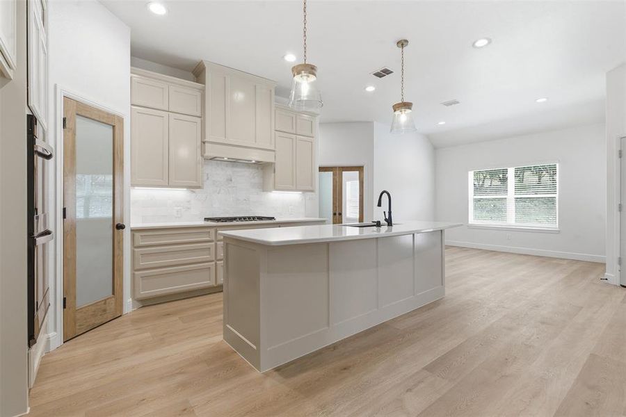Kitchen with backsplash, recessed lighting, pendant lighting, an island with sink, and light wood-style floors Kitchen with backsplash, recessed lighting, pendant lighting, an island with sink, and light wood-style floors