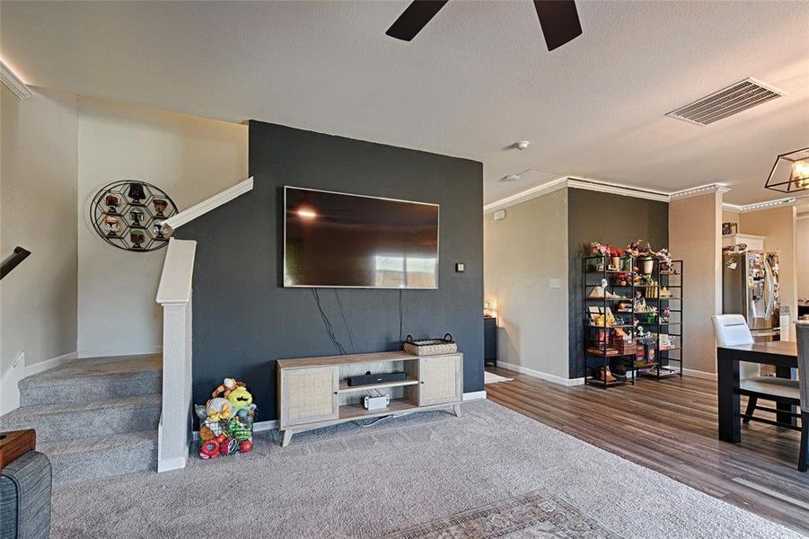 Carpeted living room featuring crown molding, stairs, and a ceiling fan Carpeted living room featuring crown molding, stairs, and a ceiling fan