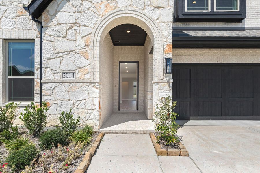 Stone and brick home exterior with arched front entry, dark garage door, and landscaped walkway