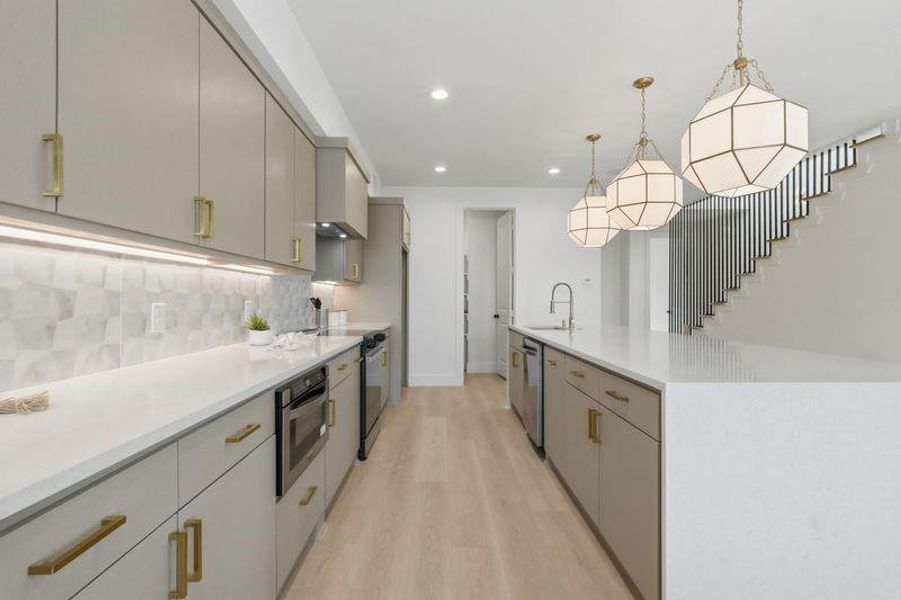 Modern kitchen featuring light gray cabinetry with gold-finish hardware, stainless steel appliances, and wood-finish flooring Modern kitchen featuring light gray cabinetry with gold-finish hardware, stainless steel appliances, and wood-finish flooring