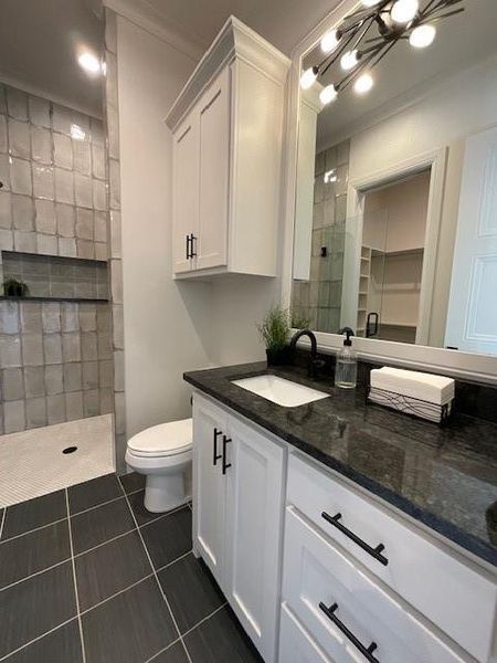 Bathroom featuring tile patterned floors, toilet, ornamental molding, vanity, and a tile shower