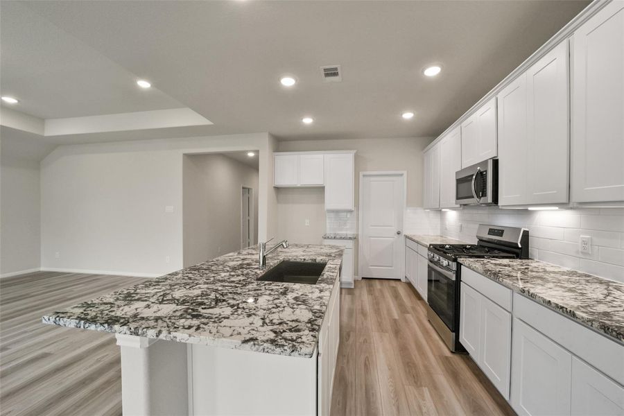 Bright modern kitchen featuring white cabinetry, granite countertops, and sleek stainless appliances.