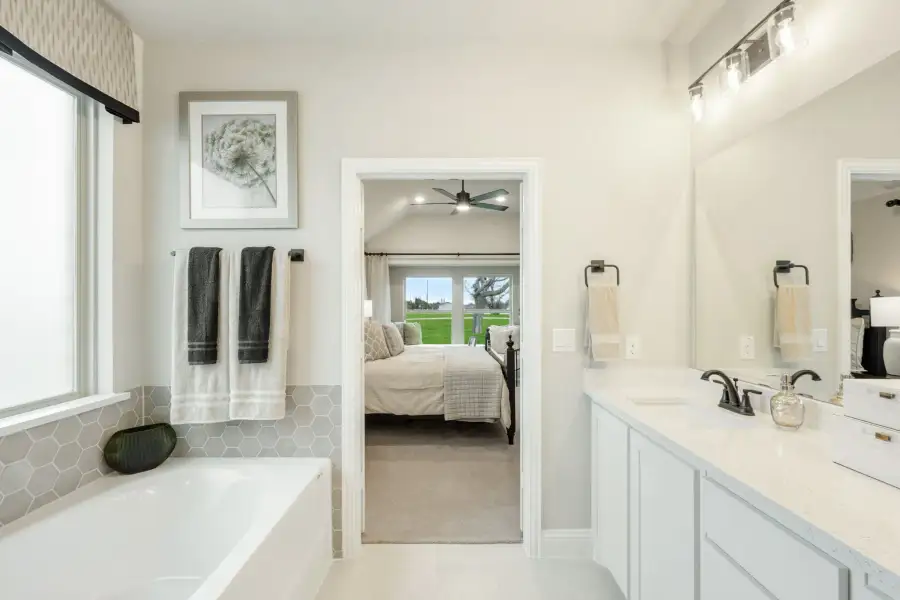 Ensuite bathroom with soaking tub, white vanity, and open doorway to master bedroom with vaulted ceiling