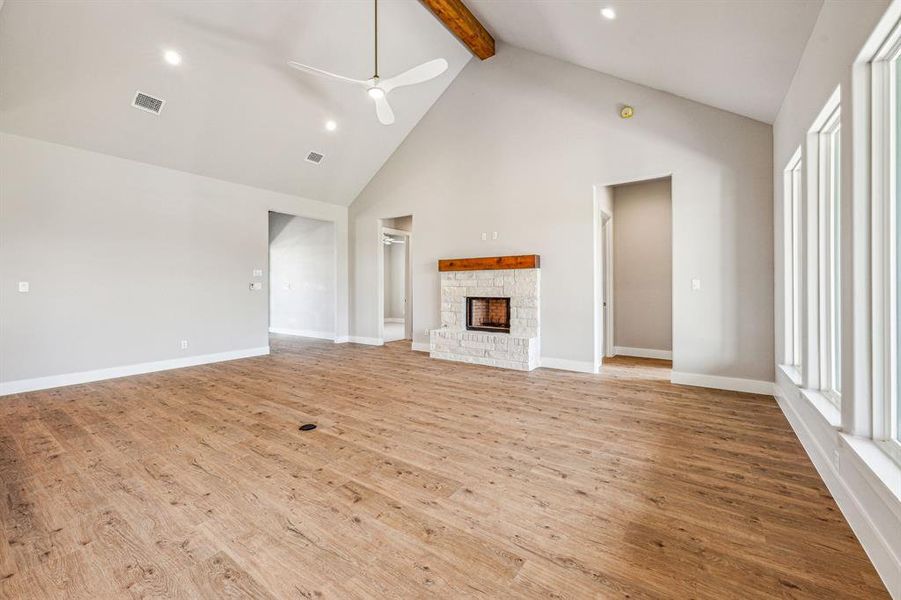 Unfurnished living room with light wood-type flooring, ceiling fan, beamed ceiling, a fireplace, and high vaulted ceiling