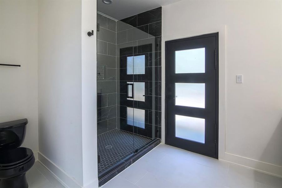 Bathroom featuring tile patterned flooring, tiled shower, and toilet