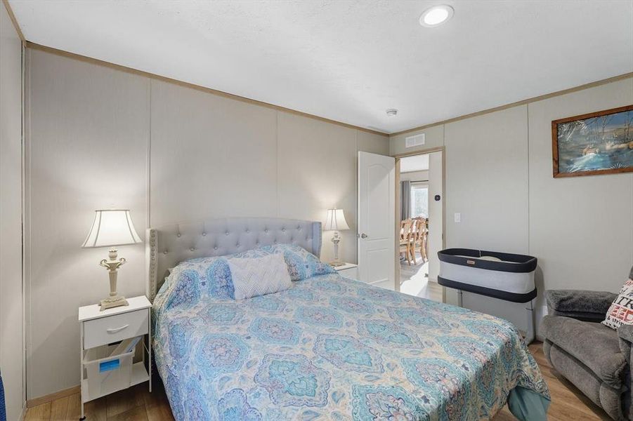 Bedroom with light wood-style flooring, ornamental molding, and a decorative wall Bedroom with light wood-style flooring, ornamental molding, and a decorative wall