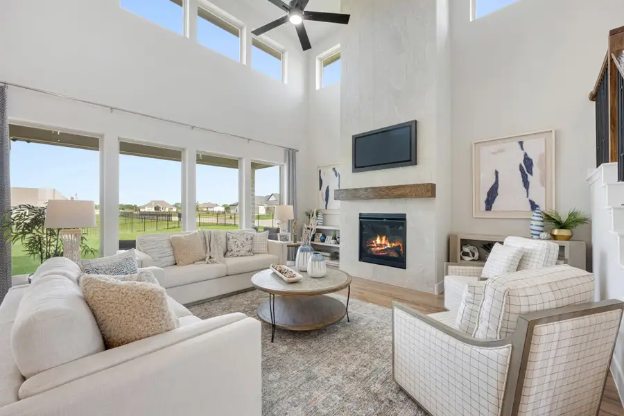 Living room with two-story ceiling, stone fireplace, ceiling fan, and large windows overlooking backyard