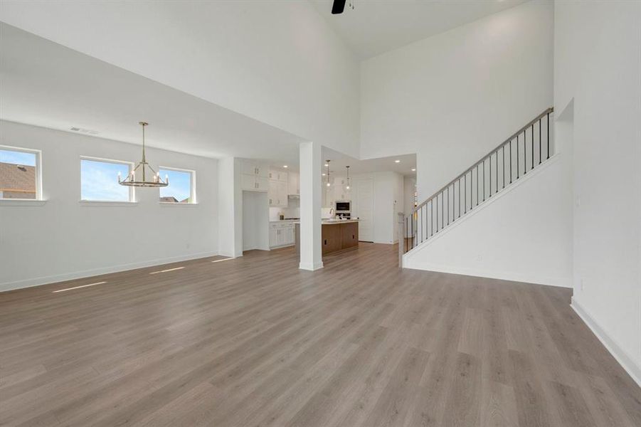 Spacious open-concept living area featuring high ceilings, wood-finish flooring, a modern chandelier, and a staircase with metal balusters