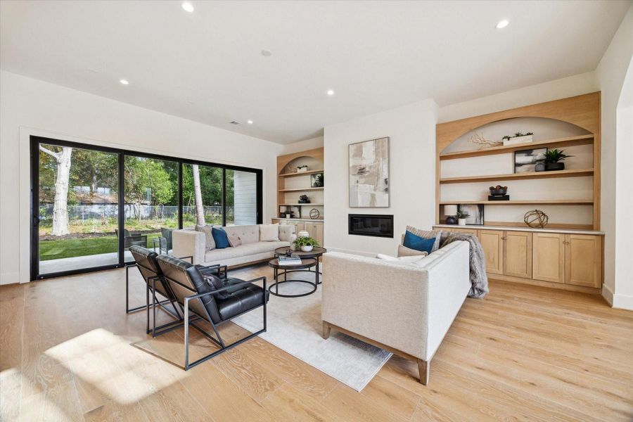 Inviting living room with custom onsite built-ins, sleek fireplace, white oak wood flooring, and large sliding doors to the backyard.