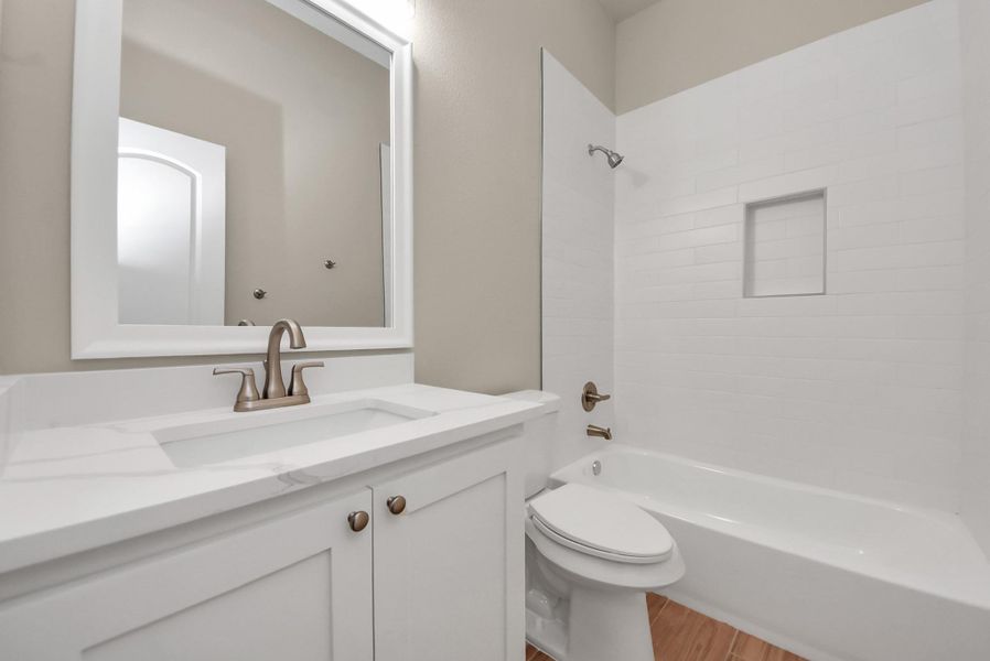 This secondary bathroom is right off the fourth bedroom and also features a sleek white vanity and countertop, updated fixtures, a large mirror, and a bathtub with a tiled shower surround.