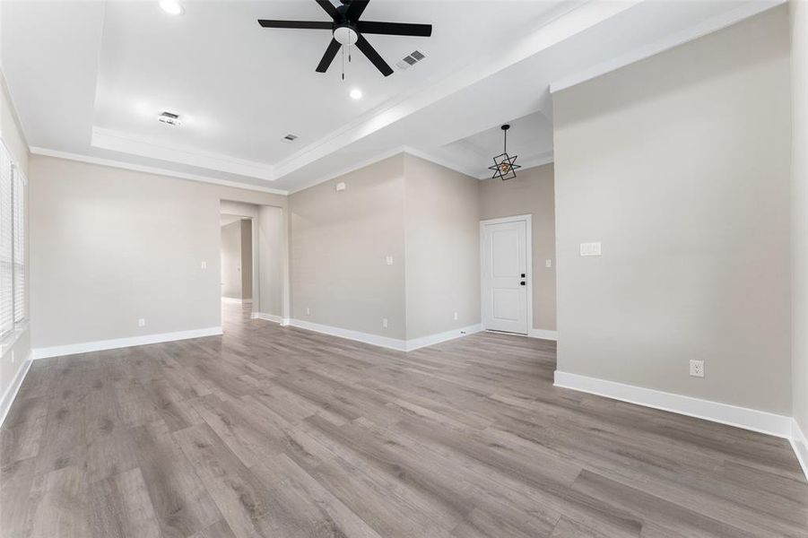 Empty room with crown molding, a raised ceiling, ceiling fan with notable chandelier, and light hardwood / wood-style flooring