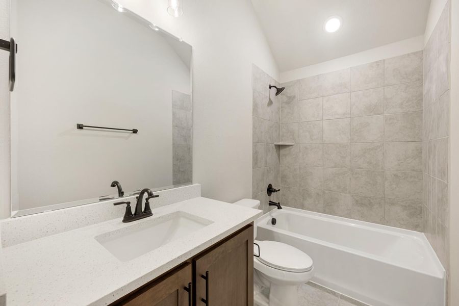 Bathroom with single vanity, white quartz countertop, tub-shower combo with gray tile surround, and dark bronze fixtures