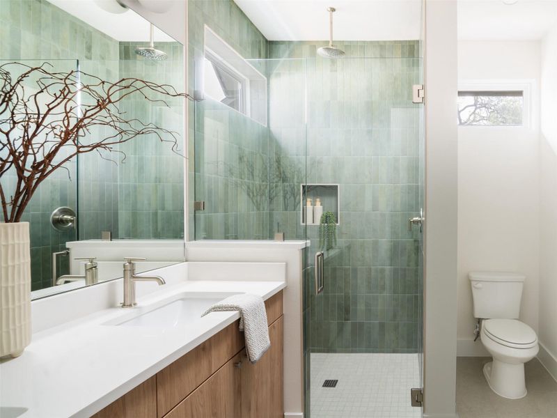 Glass-enclosed shower with green vertical tile, featuring a ceiling-mounted rain showerhead and an integrated niche
