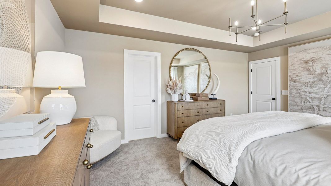 Primary suite with tray ceiling, windows, and carpet Primary suite with tray ceiling, windows, and carpet