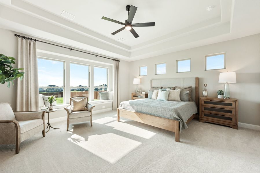 Master bedroom with tray ceiling, ceiling fan, wood bed frame, window seat, and large windows with natural light