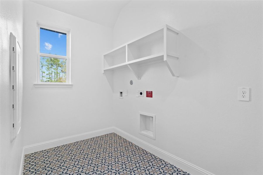 This bright and functional laundry room is conveniently located and ready for your appliances. It features clean white walls, trim, window, and shelves for storing your laundry supplies. The tile work in this laundry room is a nice feature!
