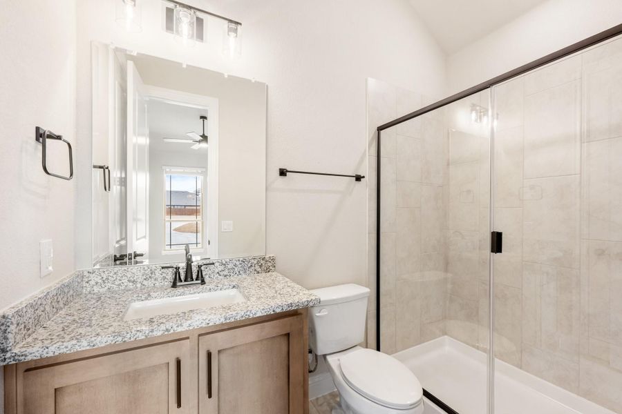 Bathroom with granite vanity, wood cabinets, glass shower, and white toilet with dark hardware accents Bathroom with granite vanity, wood cabinets, glass shower, and white toilet with dark hardware accents