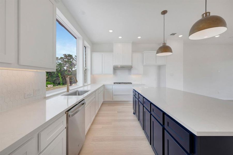 Expansive kitchen featuring a large central island with navy cabinetry, white countertops, stainless steel appliances, and wood-finish flooring