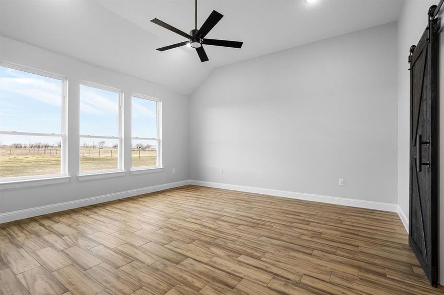 Unfurnished room featuring ceiling fan, a barn door, and vaulted ceiling