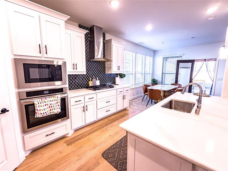 Kitchen with stainless steel appliances, light wood-type flooring, white cabinets, decorative backsplash, and recessed lighting