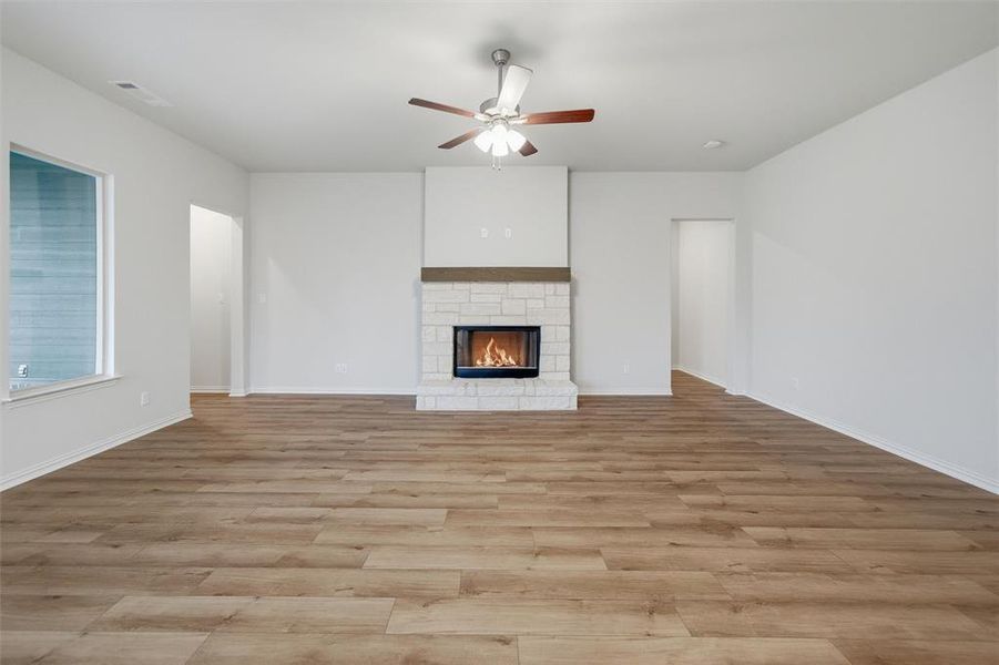 Unfurnished living room featuring a ceiling fan, light wood finished floors, and a fireplace Unfurnished living room featuring a ceiling fan, light wood finished floors, and a fireplace