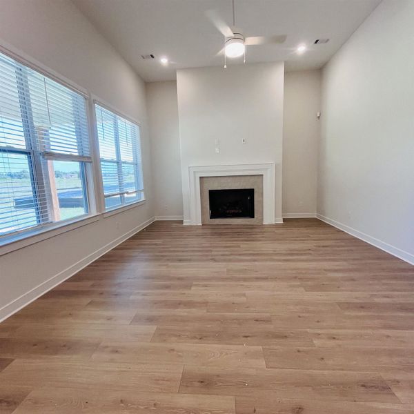 Spacious living area featuring ample natural light, a ceiling fan, recessed lighting, wood-finish flooring, and a fireplace with a stone surround Spacious living area featuring ample natural light, a ceiling fan, recessed lighting, wood-finish flooring, and a fireplace with a stone surround
