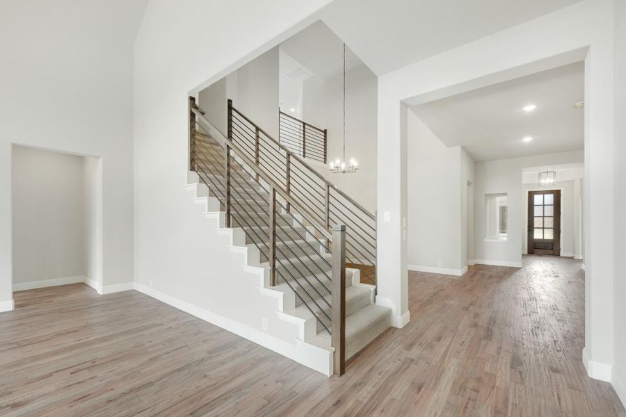 Open foyer with staircase featuring metal railings, hardwood floors, and high ceilings leading to front entry door Open foyer with staircase featuring metal railings, hardwood floors, and high ceilings leading to front entry door