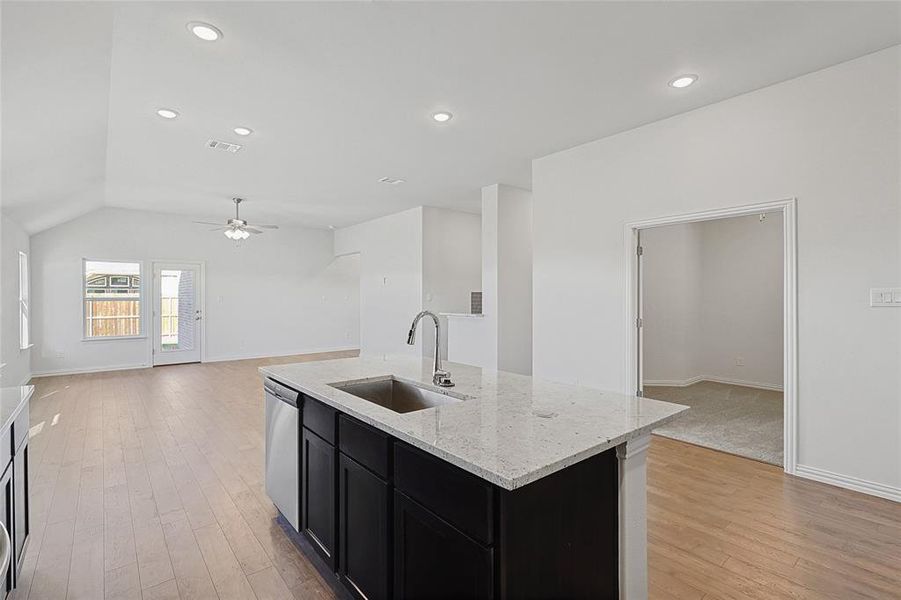 Kitchen with ceiling fan, sink, stainless steel dishwasher, vaulted ceiling, and a center island with sink