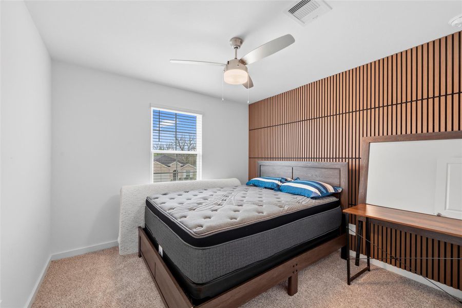 This secondary bedroom is enhanced by a designer-inspired wood accent wall with vertical detailing, paired with a streamlined layout, ceiling fan, and soft natural light. This secondary bedroom is enhanced by a designer-inspired wood accent wall with vertical detailing, paired with a streamlined layout, ceiling fan, and soft natural light.