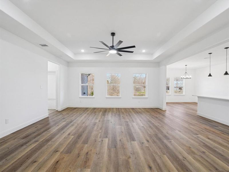 Unfurnished living room with ceiling fan, a chandelier, wood finished floors, and a tray ceiling