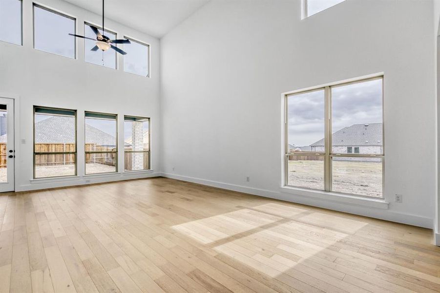 Unfurnished living room with a ceiling fan, light wood-style flooring, and a high ceiling