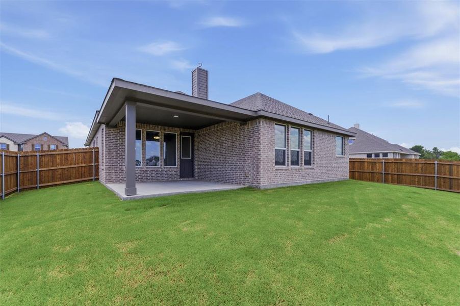 Expansive green lawn surrounds a brick exterior home featuring a covered concrete patio, wood privacy fencing, and multiple windows Expansive green lawn surrounds a brick exterior home featuring a covered concrete patio, wood privacy fencing, and multiple windows
