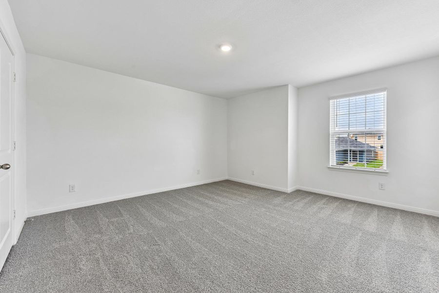 Spacious room featuring neutral paint, gray patterned carpeting, a single window with blinds, a white paneled door, and recessed lighting