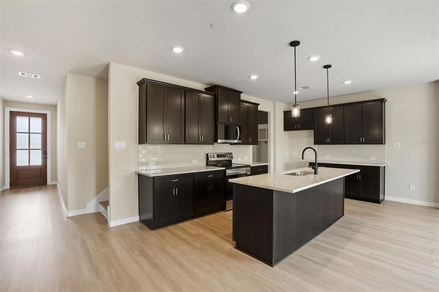 Kitchen with backsplash, appliances with stainless steel finishes, pendant lighting, light stone countertops, and light wood-type flooring Kitchen with backsplash, appliances with stainless steel finishes, pendant lighting, light stone countertops, and light wood-type flooring