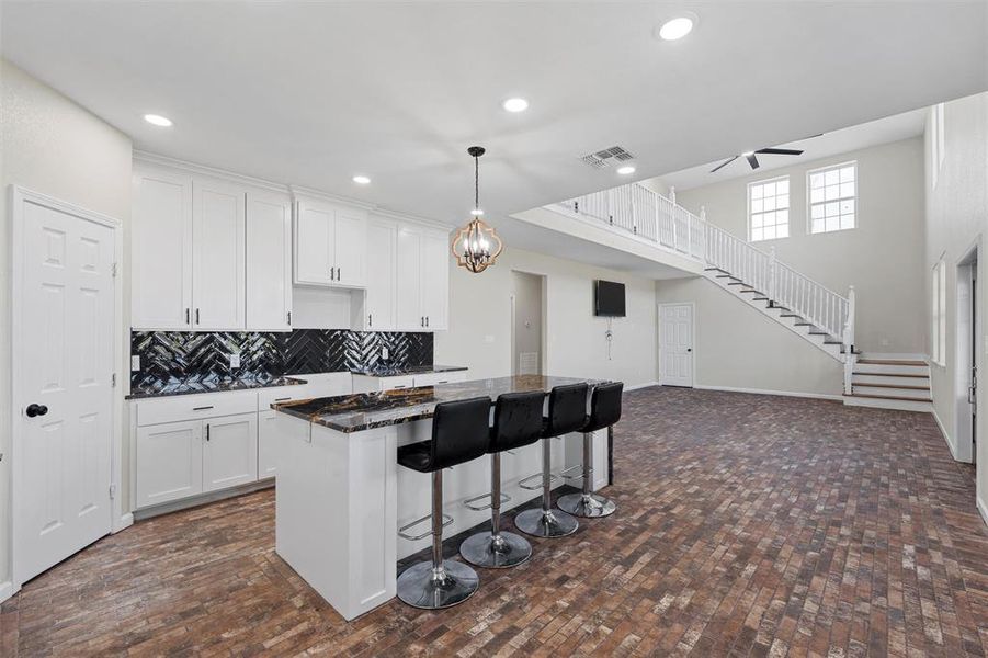 Kitchen with tasteful backsplash, white cabinetry, a kitchen island, a breakfast bar area, and a towering ceiling Kitchen with tasteful backsplash, white cabinetry, a kitchen island, a breakfast bar area, and a towering ceiling