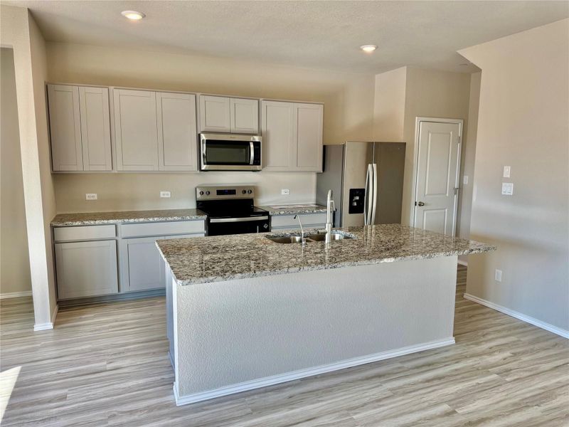 Kitchen featuring light stone counters, appliances with stainless steel finishes, an island with sink, light wood-style floors, and recessed lighting