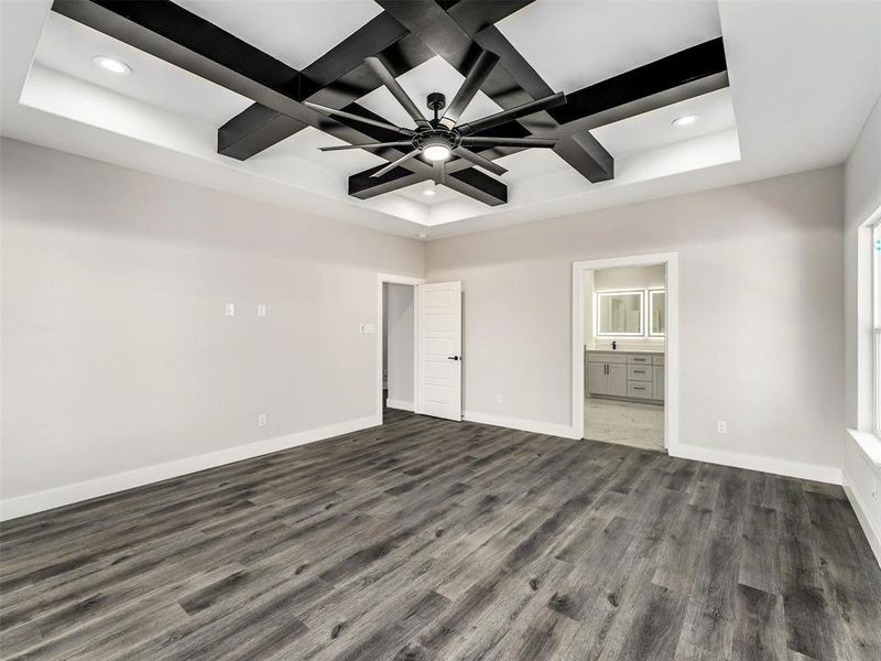 Unfurnished bedroom with coffered ceiling, dark wood-style flooring, beamed ceiling, ensuite bath, and ceiling fan Unfurnished bedroom with coffered ceiling, dark wood-style flooring, beamed ceiling, ensuite bath, and ceiling fan