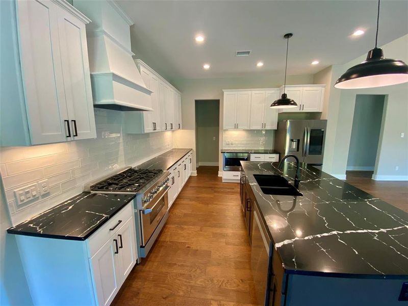 Kitchen with tasteful backsplash, custom exhaust hood, hanging light fixtures, hardwood / wood-style flooring, and appliances with stainless steel finishes