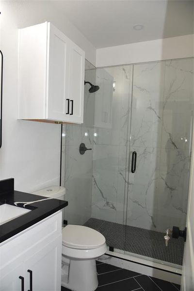 Bathroom featuring tile patterned flooring, vanity, a shower with door, and toilet